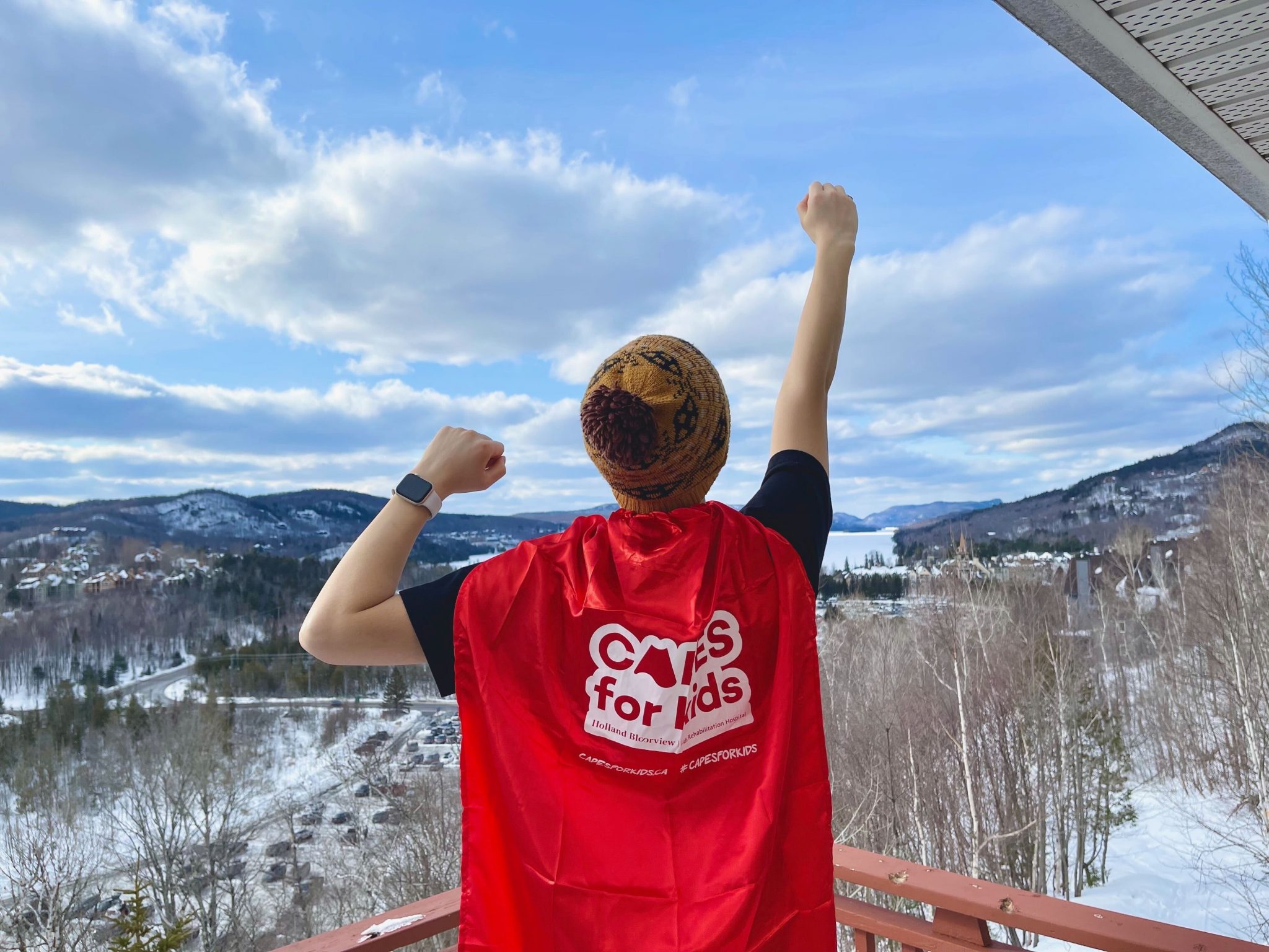 Jarvis Consulting Group team member wearing a Capes for Kids cape, one of our charitable partners, while holding fist up to the sky with mountains in the background